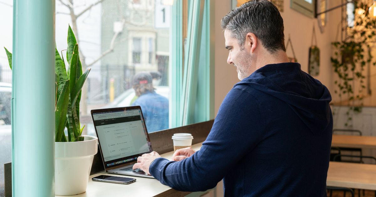 Person working on laptop in café using facility management software interface for building operations