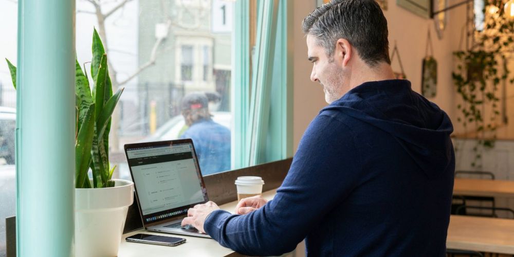 Person working on laptop in café using facility management software interface for building operations